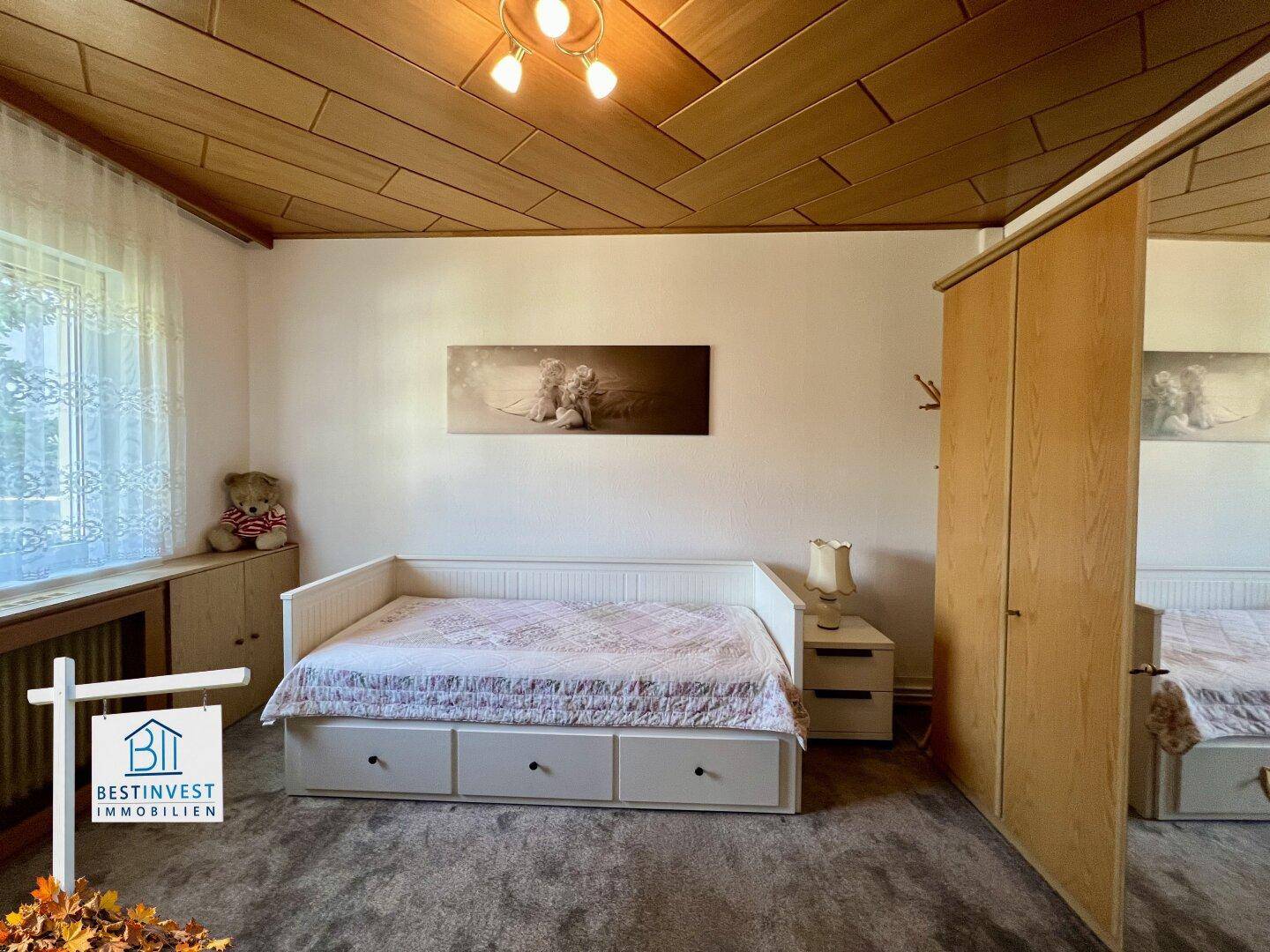 Gemütliches Schlafzimmer mit Holztäfeldecke, Einzelbett und Kleiderschrank, hell durch großes Fenster.