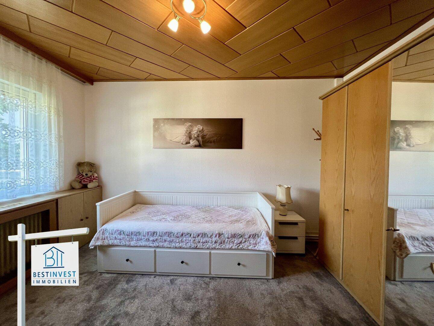 Helles Schlafzimmer mit Holzpaneeldecke, Teppichboden und einem Bett mit integriertem Stauraum.