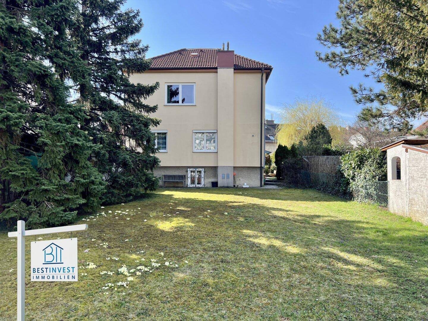 Rückansicht des Wohnhauses mit großem Garten, hohen Bäumen und einer kleinen Gartenhütte.