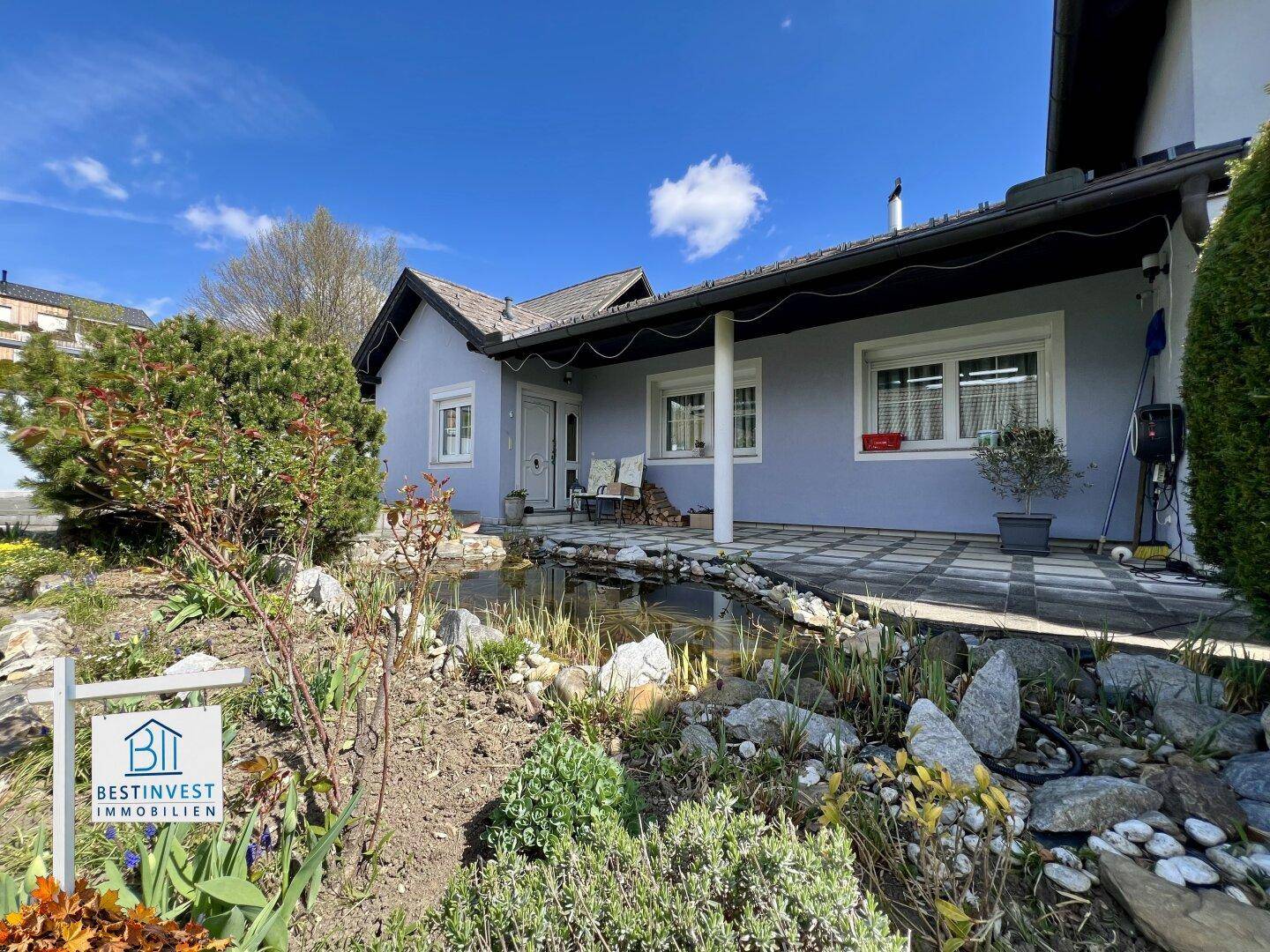 Seitenansicht des Hauses mit einer gemütlichen Terrasse und einem kleinen Teich im gepflegten Garten.