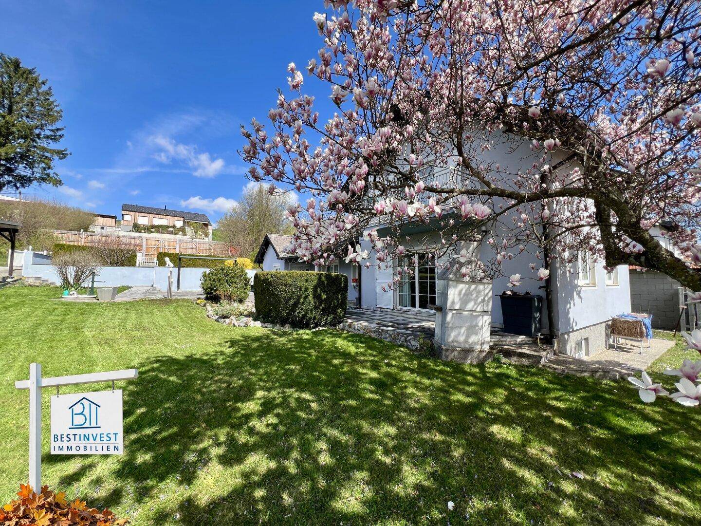 Rückansicht des Hauses vom weitläufigen Garten aus, umgeben von blühenden Bäumen im Frühling.