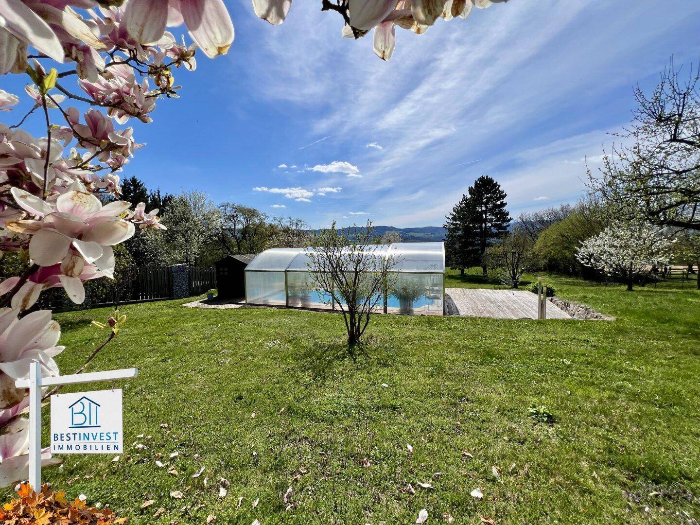 Großer Gartenbereich mit einem überdachten Swimmingpool und weitem Blick in die umliegende Natur.