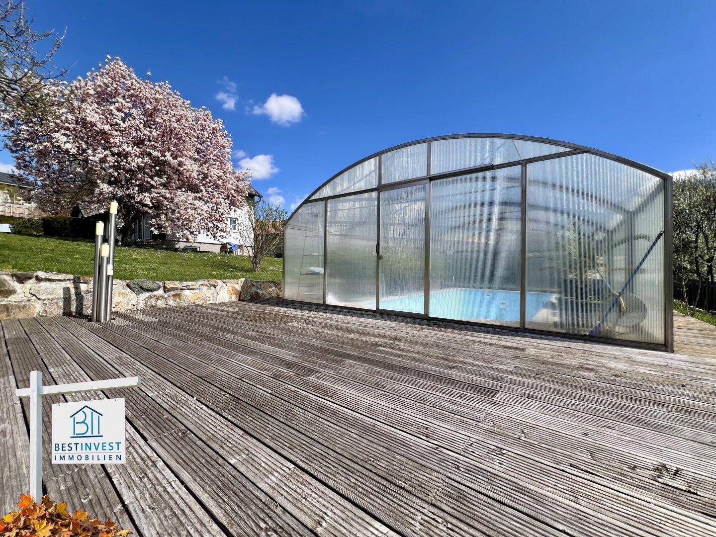 Geräumige Holzterrasse neben dem überdachten Swimmingpool, ideal für Entspannung im Freien.