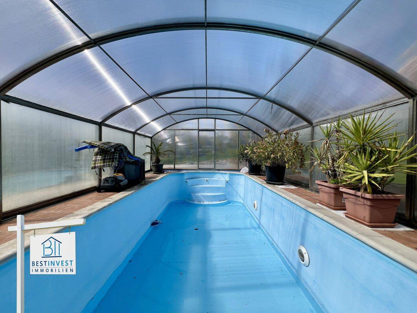 Innenansicht des überdachten Pools mit Pflanzen und blauer Wasseroberfläche.