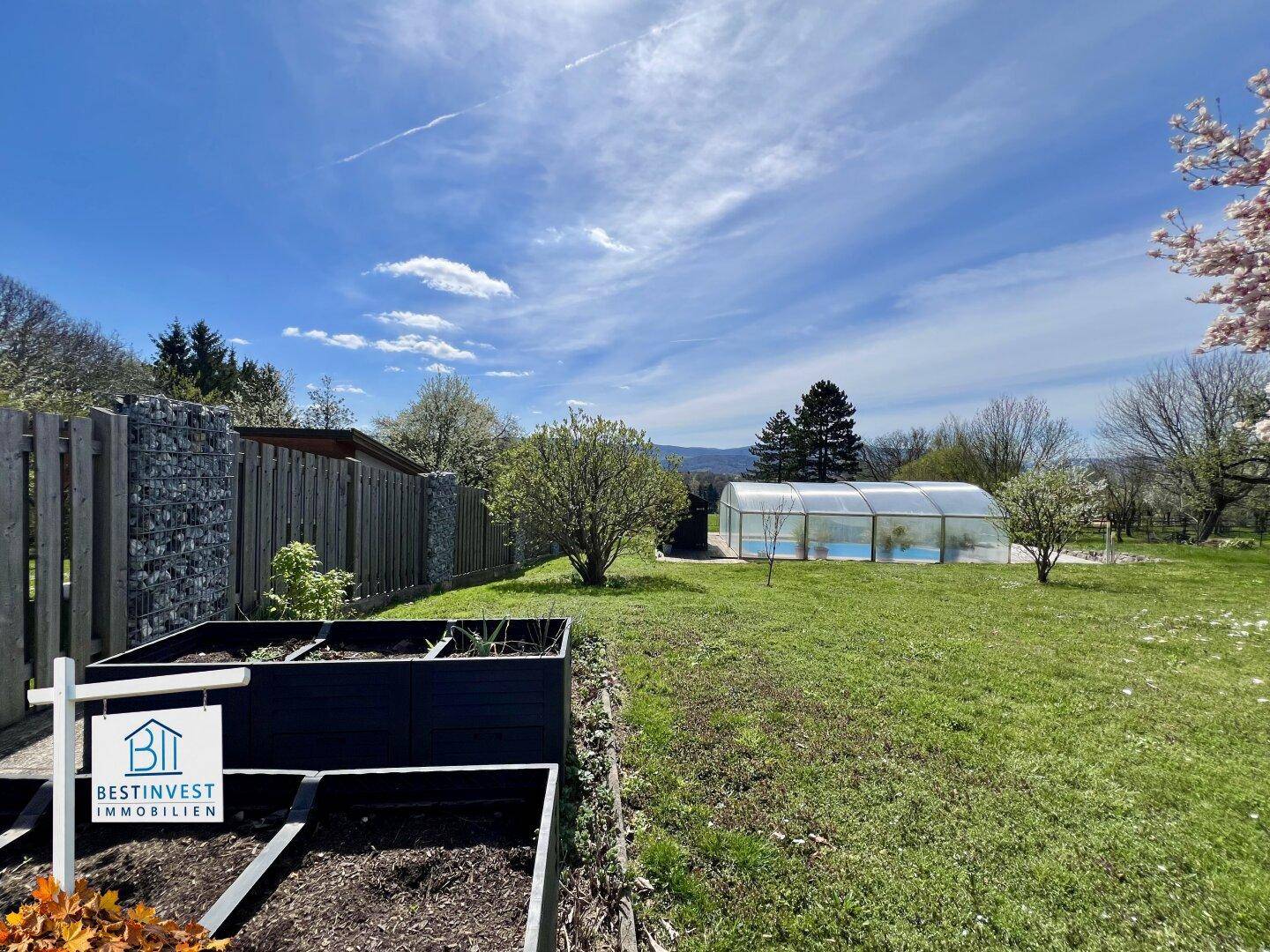 Großer Gartenbereich mit Hochbeeten und einem überdachten Pool im Hintergrund.