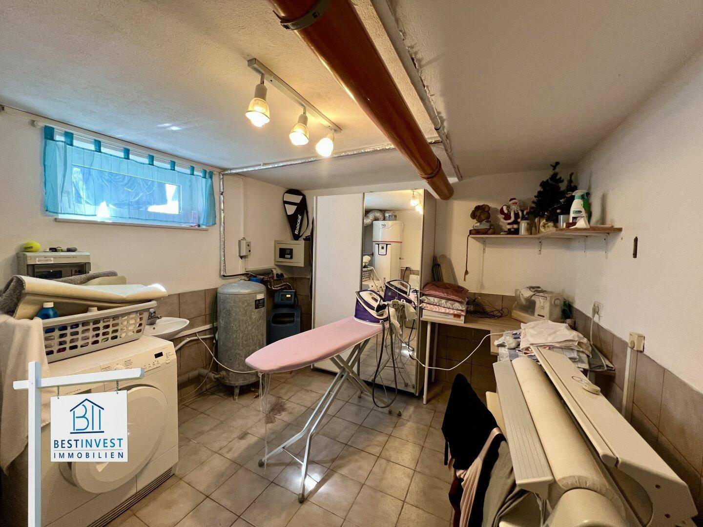 Waschküche im Keller mit Waschmaschine, Bügelbrett und Fenster für Belüftung.