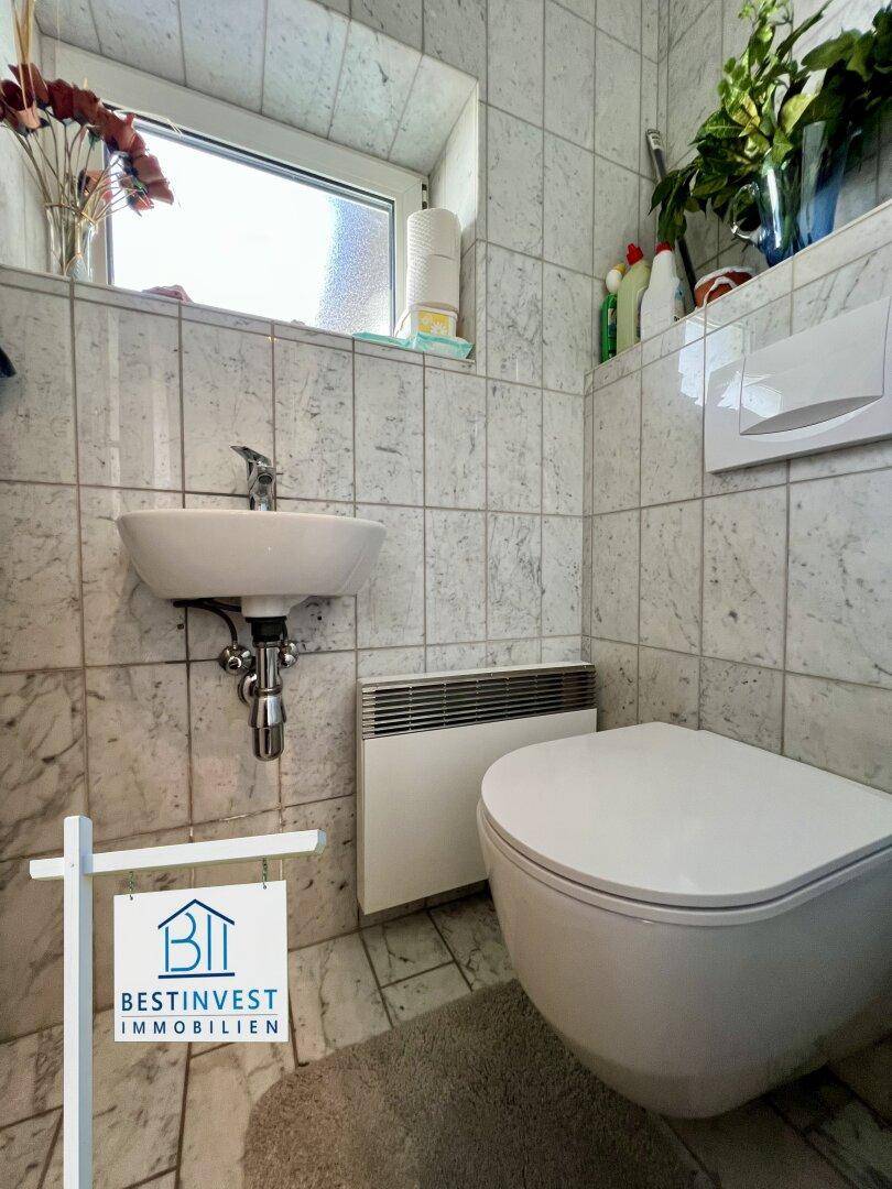 Kleines Gäste-WC mit Wand-WC, Handwaschbecken und Fenster für Belüftung.