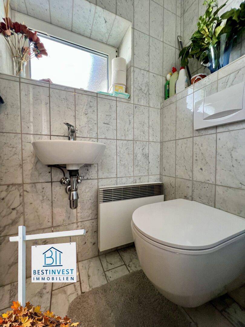 Kleines Gäste-WC mit wandhängendem WC, Handwaschbecken und Fenster, vollständig gefliest.