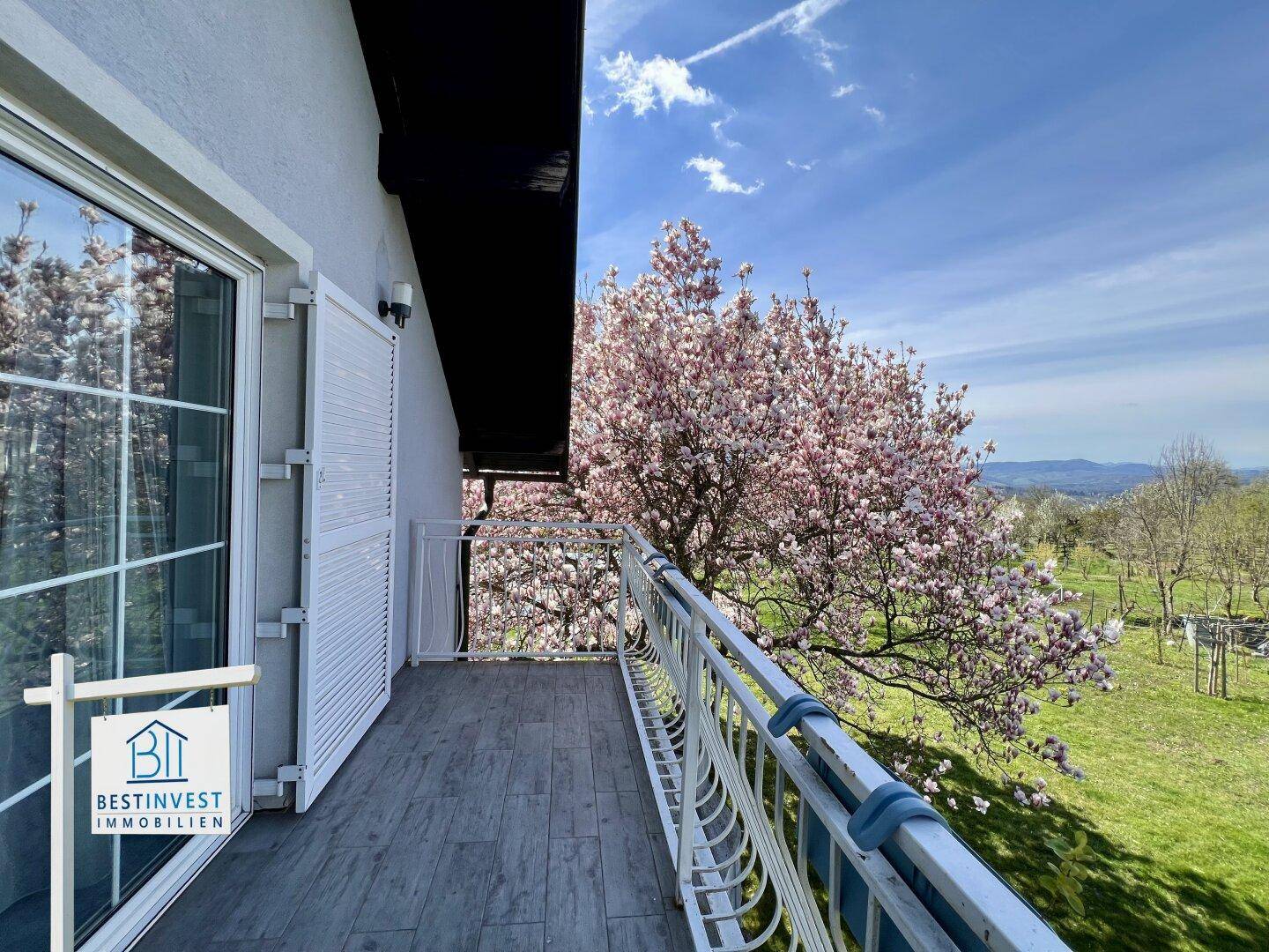 Balkon mit Holzboden und weitem Blick ins Grüne, umgeben von blühenden Bäumen.
