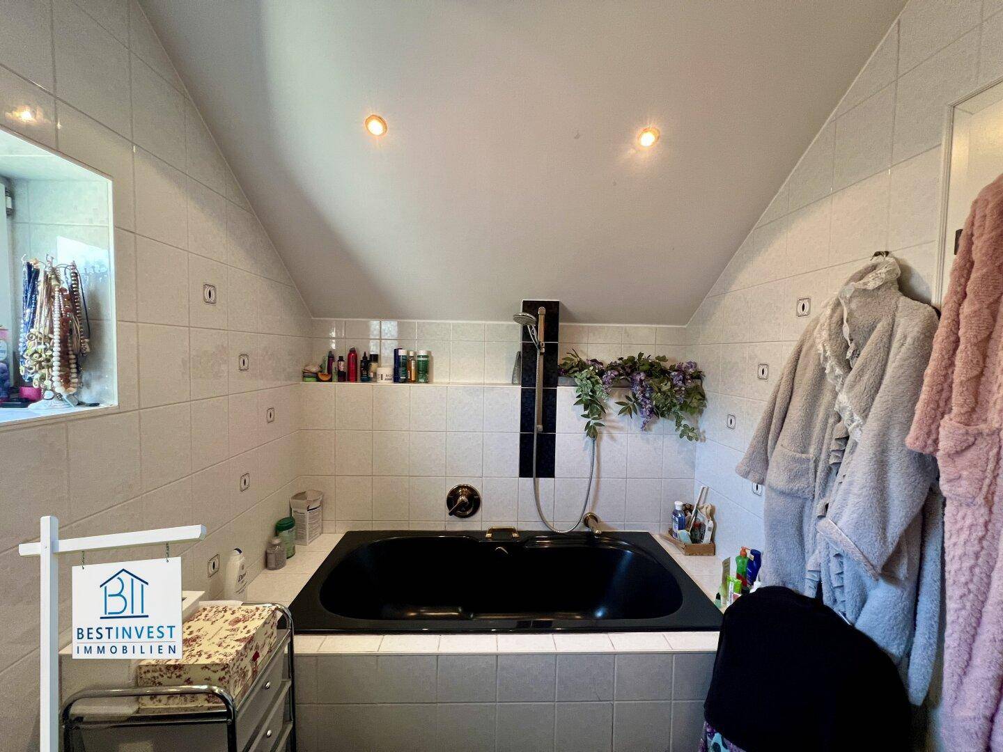Badezimmer mit schwarzer Einbaubadewanne und weißen Fliesen unter einer Dachschräge.