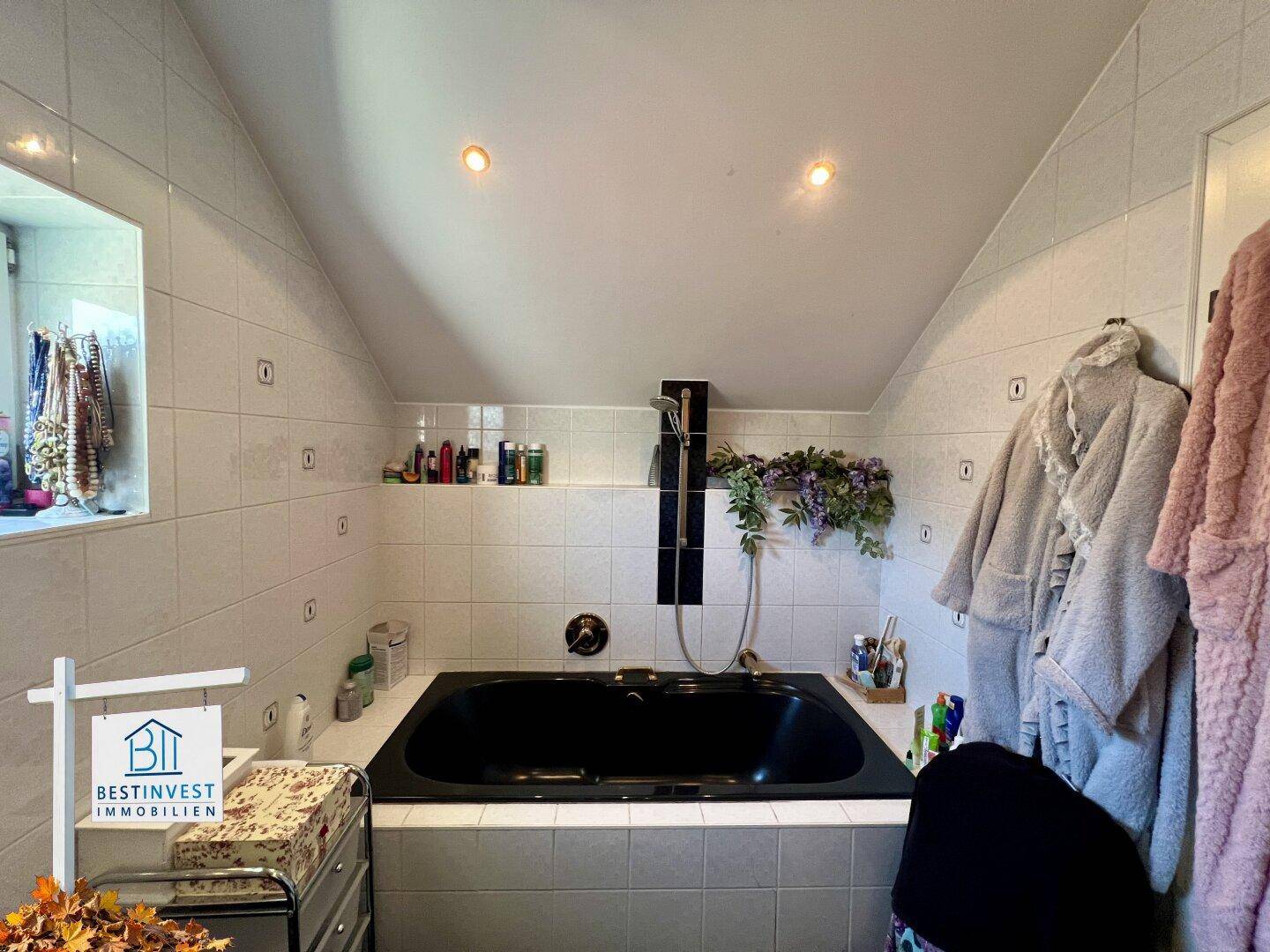 Badezimmer mit schwarzer Einbauwanne, weißen Fliesen und Dachschräge, ausgestattet mit Einbaustrahlern.