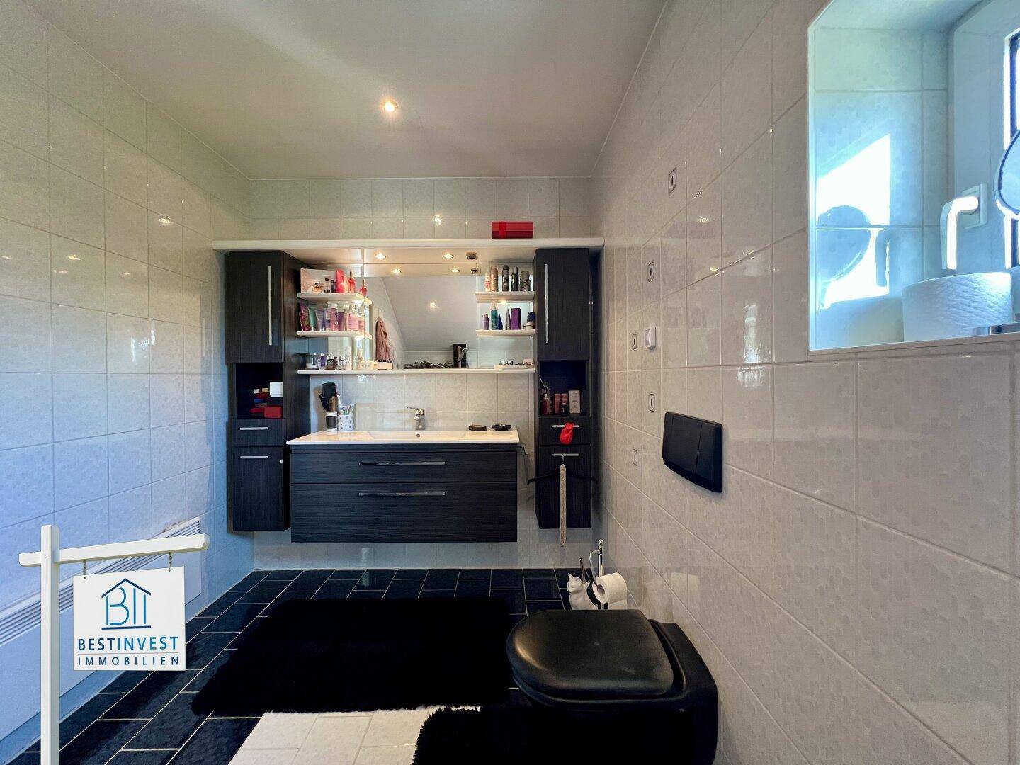 Modern gefliestes Badezimmer mit dunklem Waschtischunterschrank und Wand-WC.