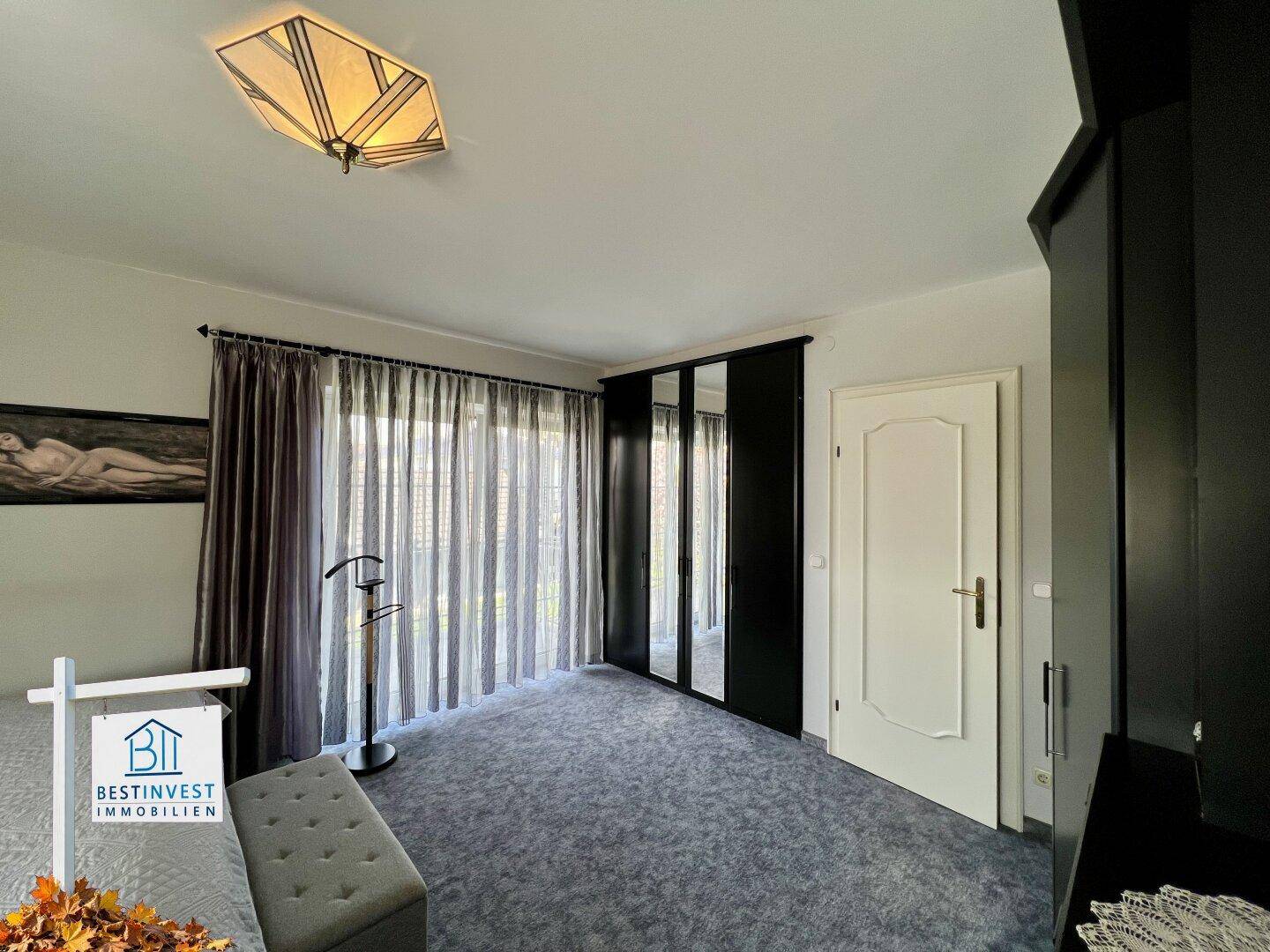 Gemütliches Schlafzimmer mit Teppichboden, großem Kleiderschrank und Vorhängen am Fenster.