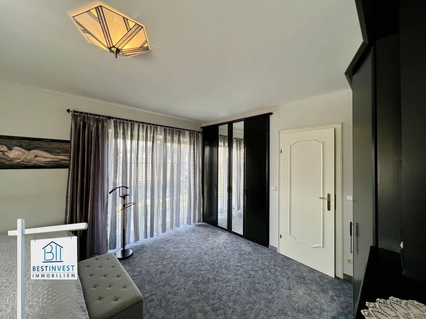 Geräumiges Schlafzimmer mit Teppichboden, großem Kleiderschrank und Zugang zu einem Fensterbereich.