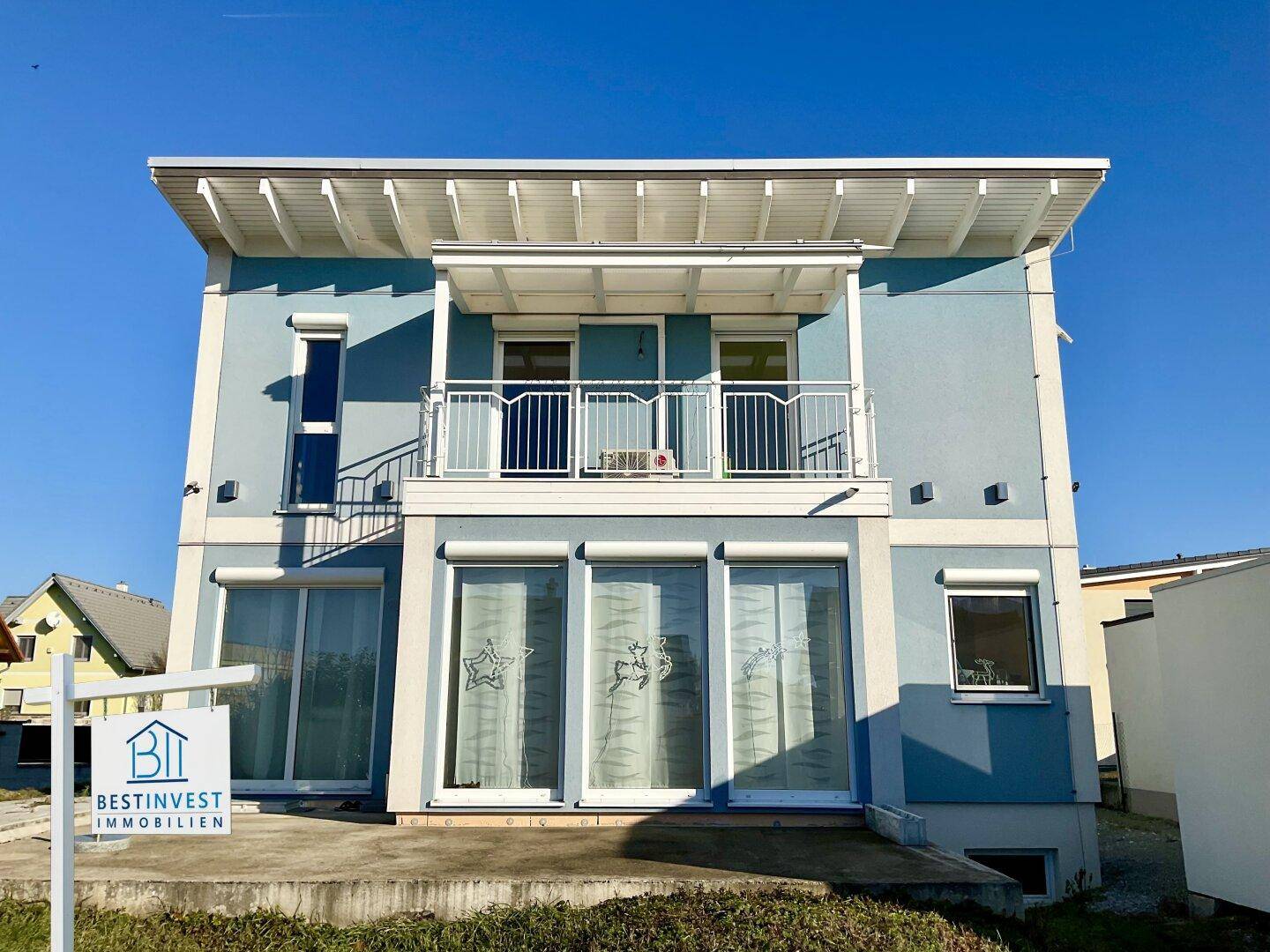 Vorderansicht des modernen Hauses mit blauer Fassade, Balkon und großen Fenstern.