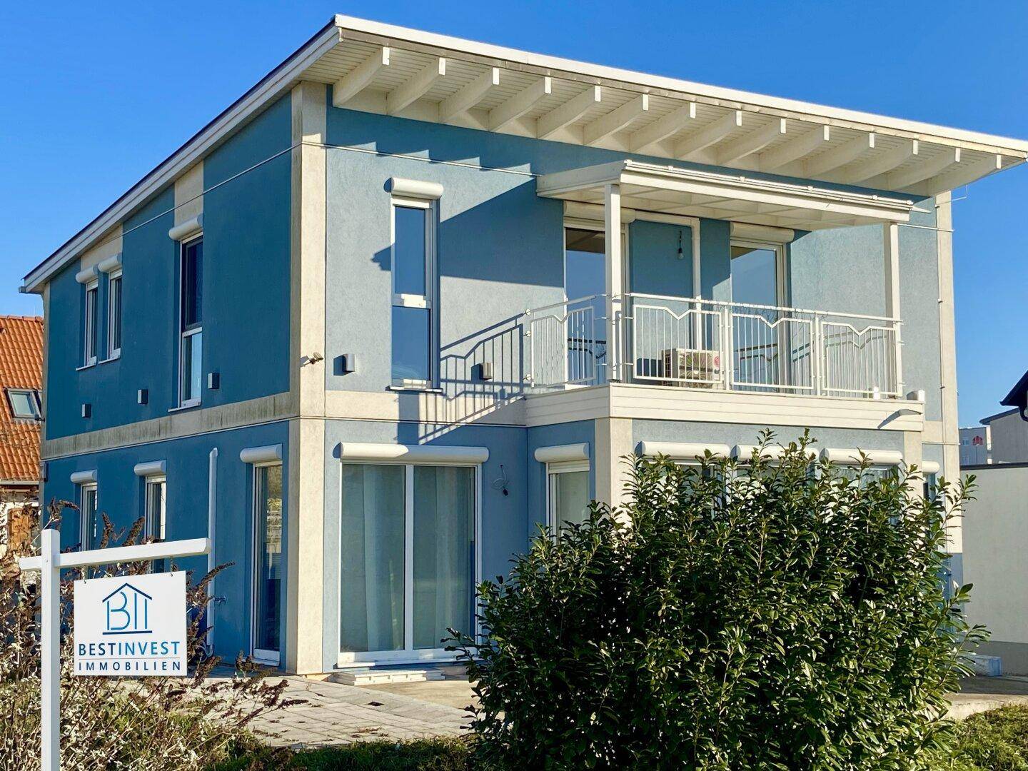 Ansicht des modernen Hauses mit blauer Fassade, Balkon und großen Fenstern im Sonnenlicht.