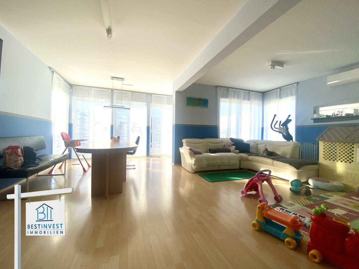 Heller, offener Wohn-Essbereich mit Holzboden, großen Fenstern und Kinderspielbereich.