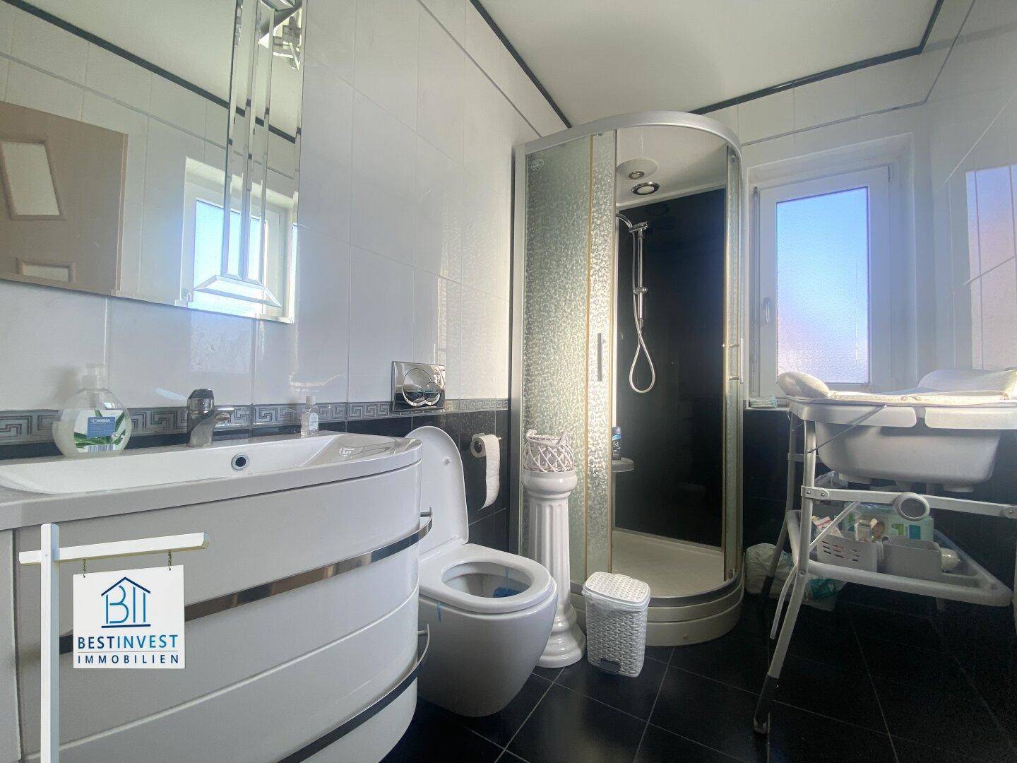 Modernes Badezimmer mit dunklen Fliesen, Dusche, Einzelwaschbecken und Fenster.