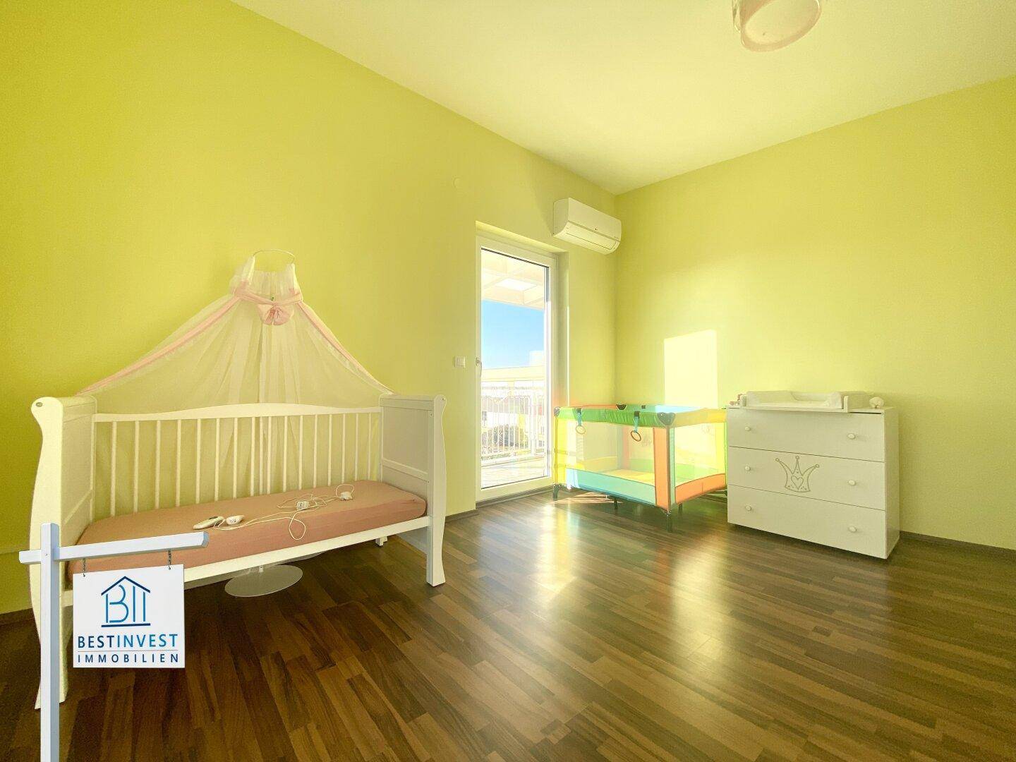 Freundliches Kinderzimmer mit Holzboden, Balkonzugang und hellgrünen Wänden.