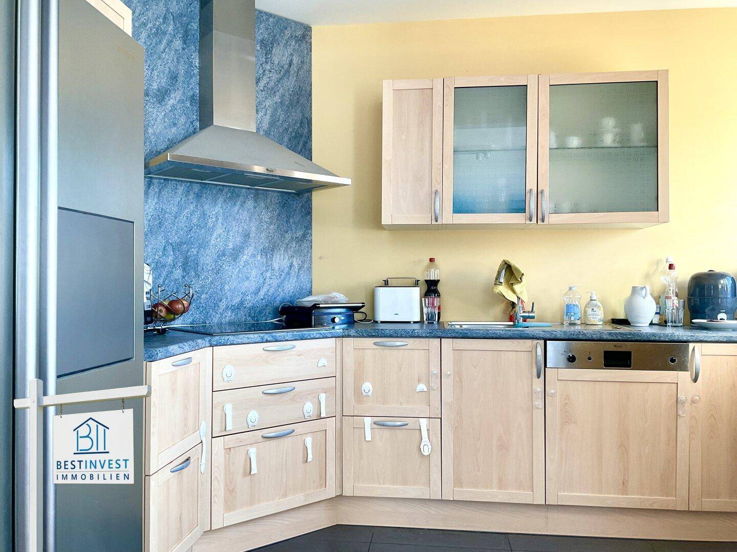 Moderne Küche mit hellen Holzschränken, Dunstabzugshaube und Kühlschrank.