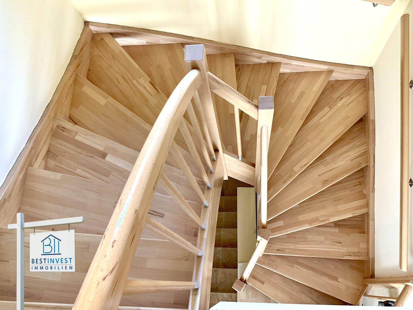 Elegante Holztreppe mit geschwungenem Geländer, die verschiedene Etagen miteinander verbindet.