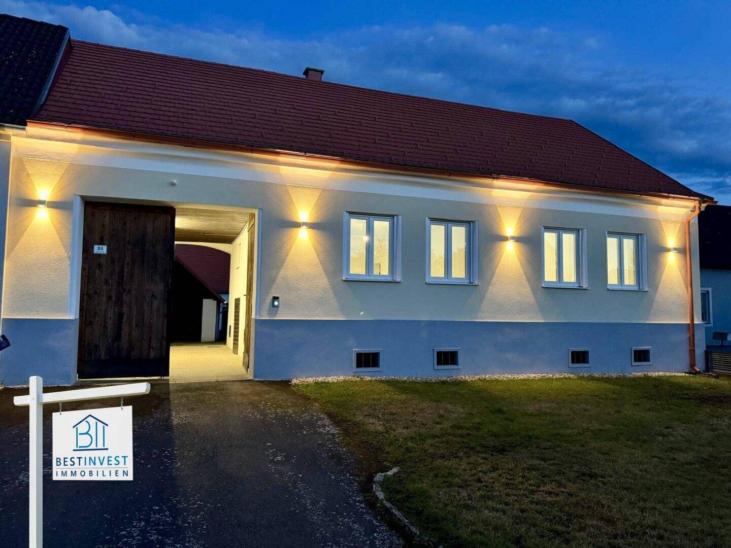 Beleuchtete Fassade des Hauptgebäudes in der Abenddämmerung mit großen Holztoren und Fenstern.