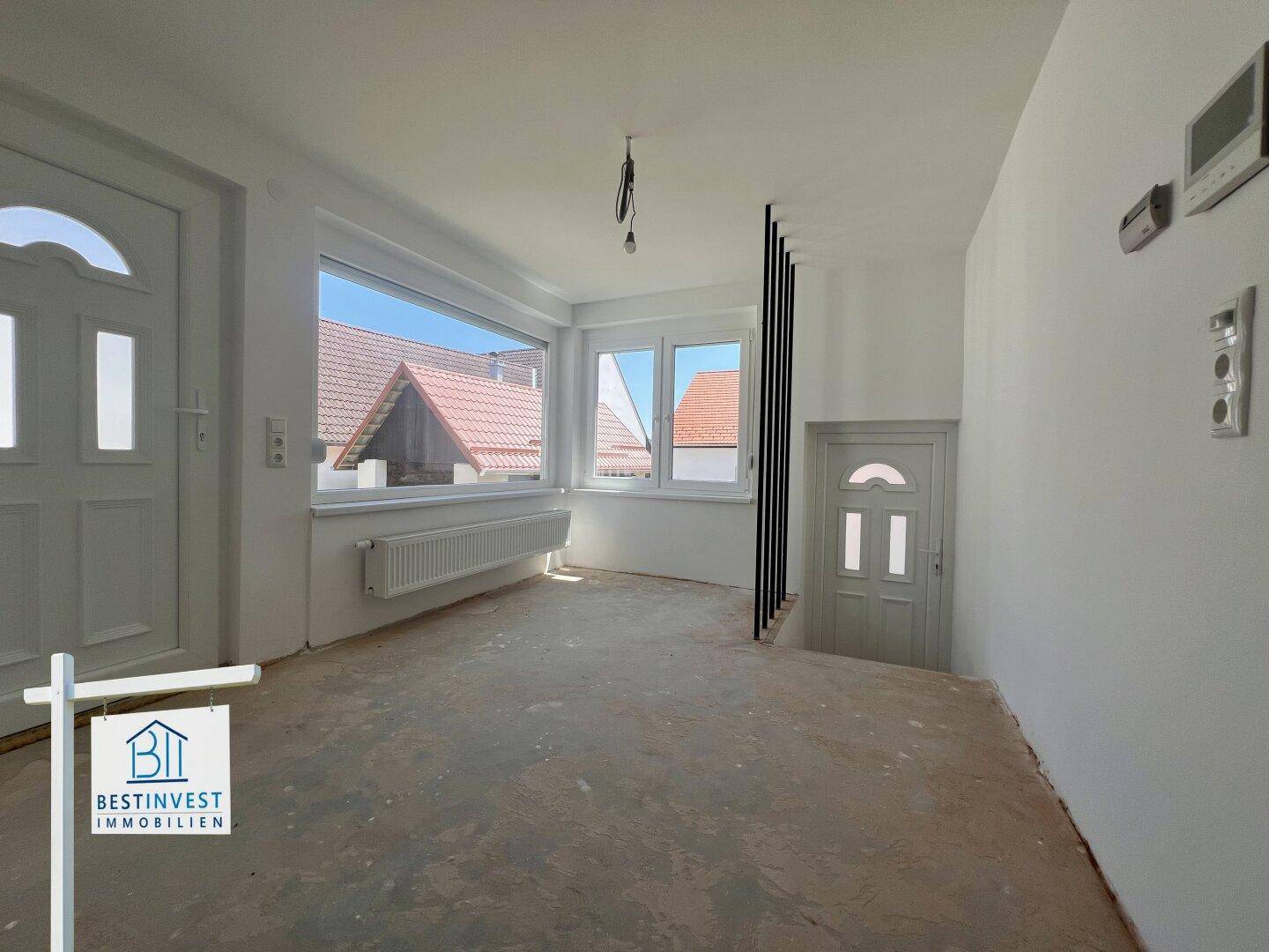 Heller Innenraum im Rohbauzustand mit großen Fenstern und zwei Türen, bereit für den Ausbau.