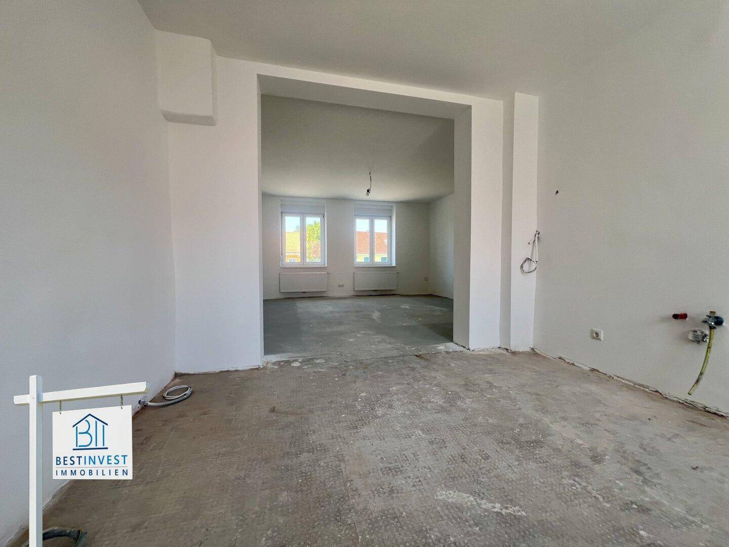 Geräumiger Innenraum im Rohbau mit offenem Durchgang zu einem weiteren Zimmer, ideal für Wohn-Essbereich.