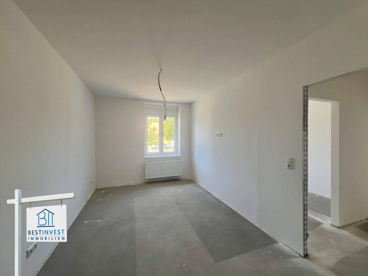 Schlichtes Zimmer im Rohbau mit einem Fenster und weiß gestrichenen Wänden, bereit für die Einrichtung.