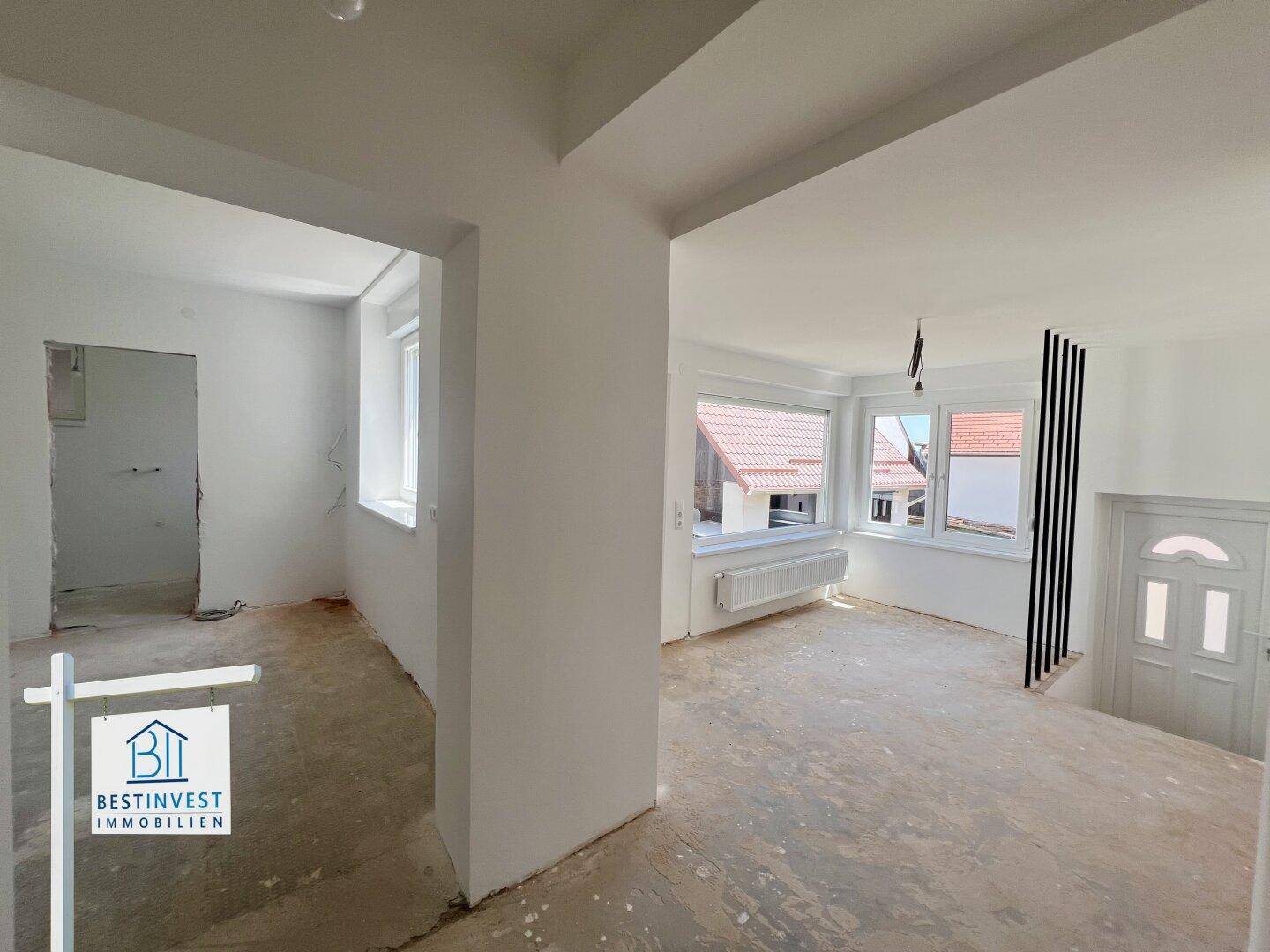 Eingangsbereich im Rohbau mit Fenstern, Treppenaufgang und offenem Zugang zu weiteren Zimmern.