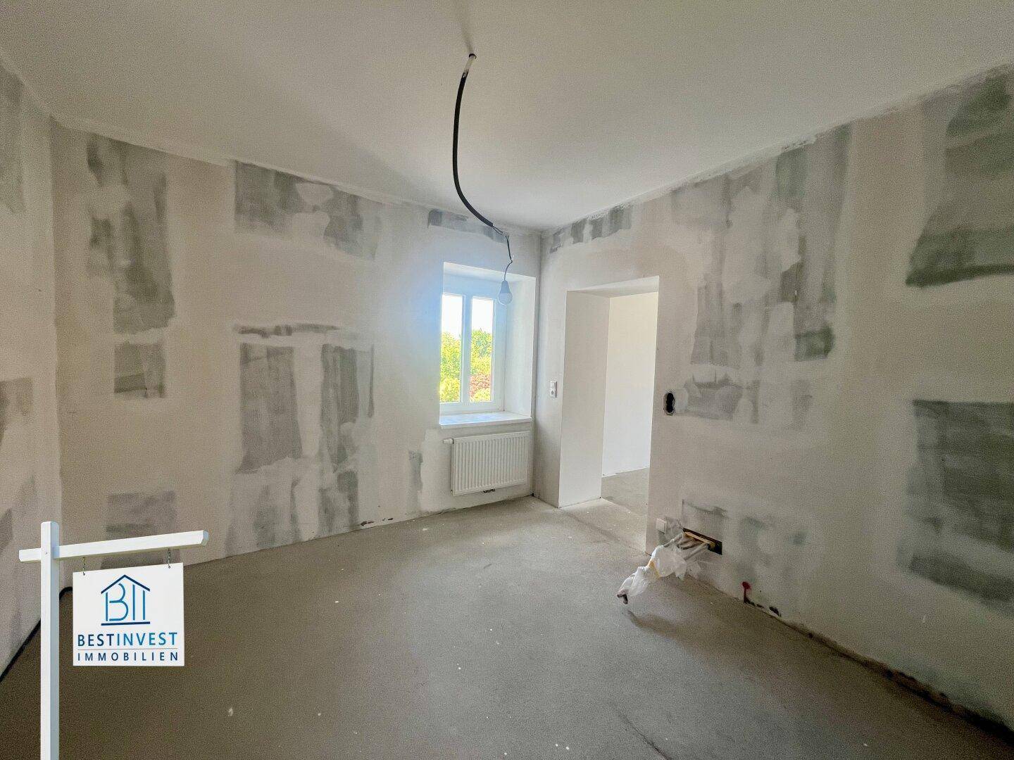 Unfertiges Zimmer im Rohbau mit sichtbaren Putzspuren und einem Fenster, wartet auf den Endausbau.