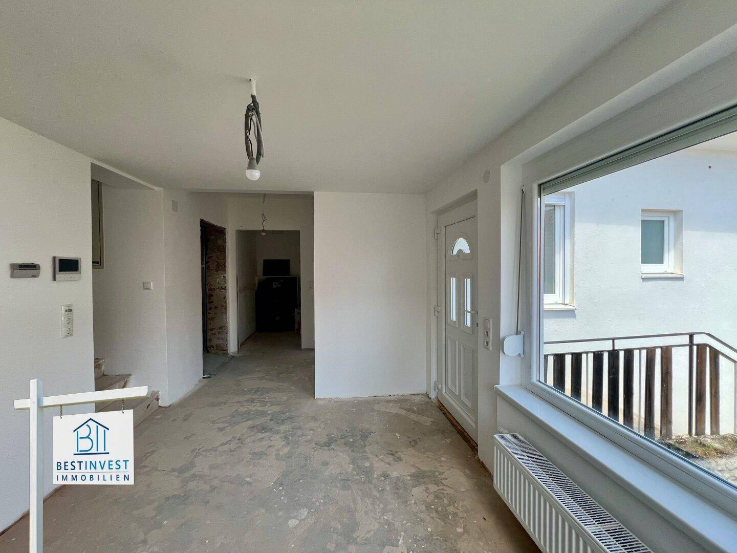 Heller Eingangsbereich im Rohbau mit großer Fensterfront und weißer Eingangstür, offen gestaltet.