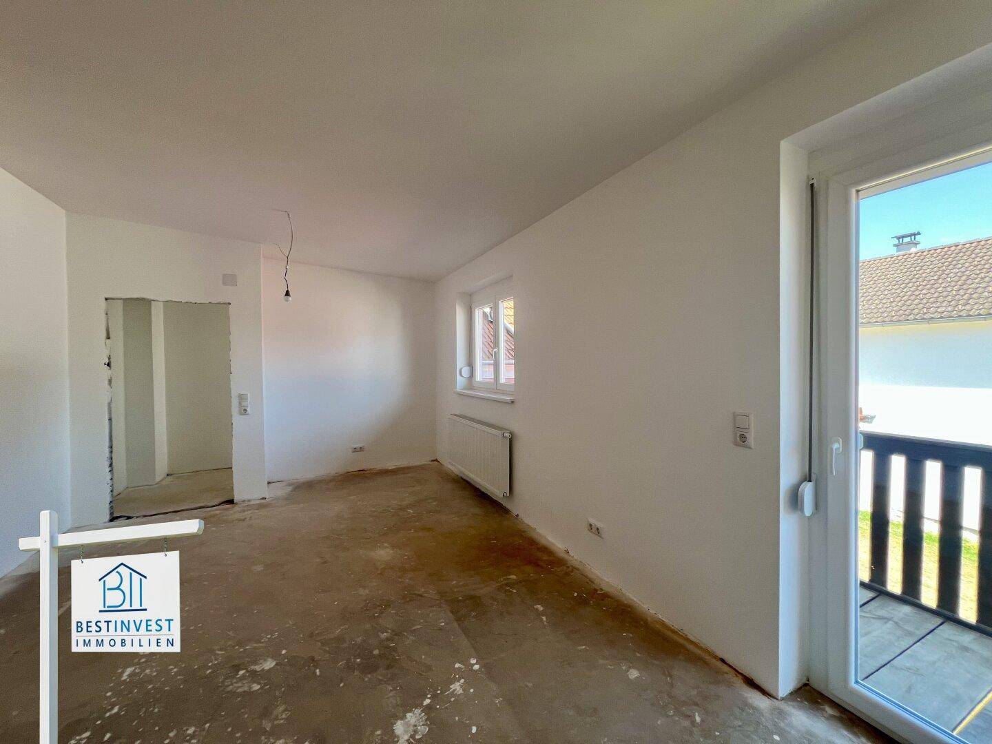 Helles Zimmer im Rohbau mit Fenster und Balkontür, bietet direkten Zugang zum Außenbereich.
