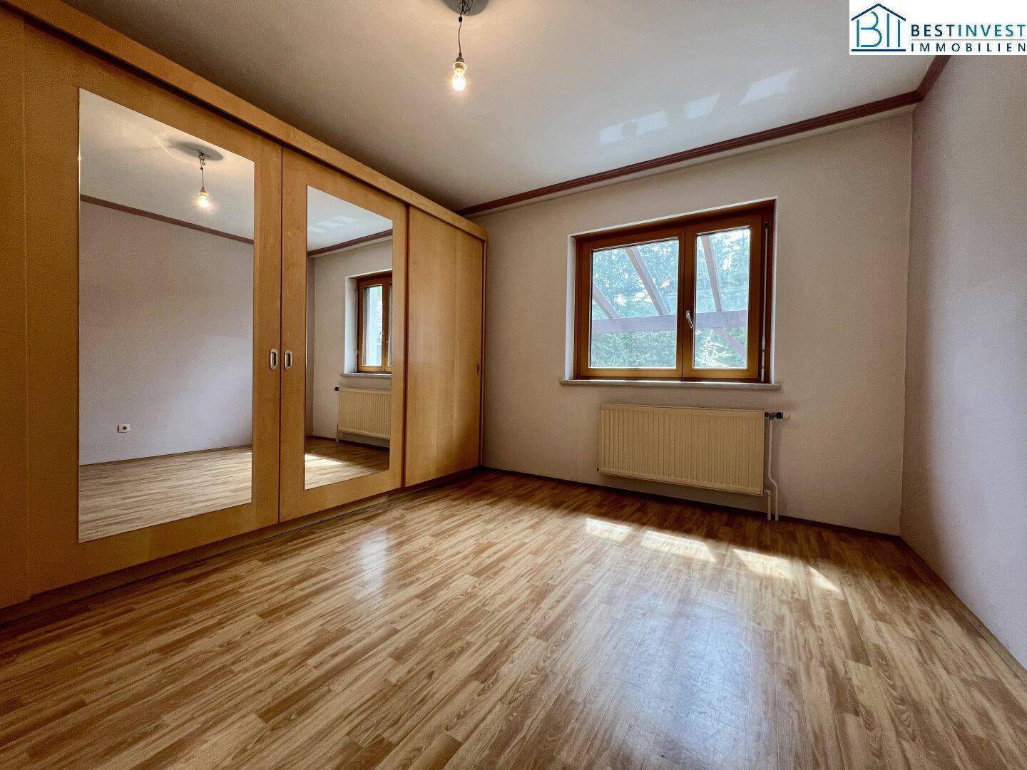 Helles Schlafzimmer mit Laminatboden und einem großen Spiegelschrank, bietet viel Stauraum.