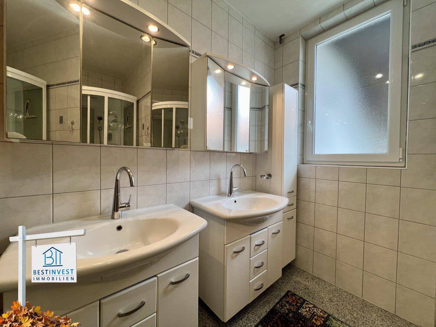 Helles Badezimmer mit Doppelwaschbecken, Spiegelschränken und einem Fenster für Tageslicht.