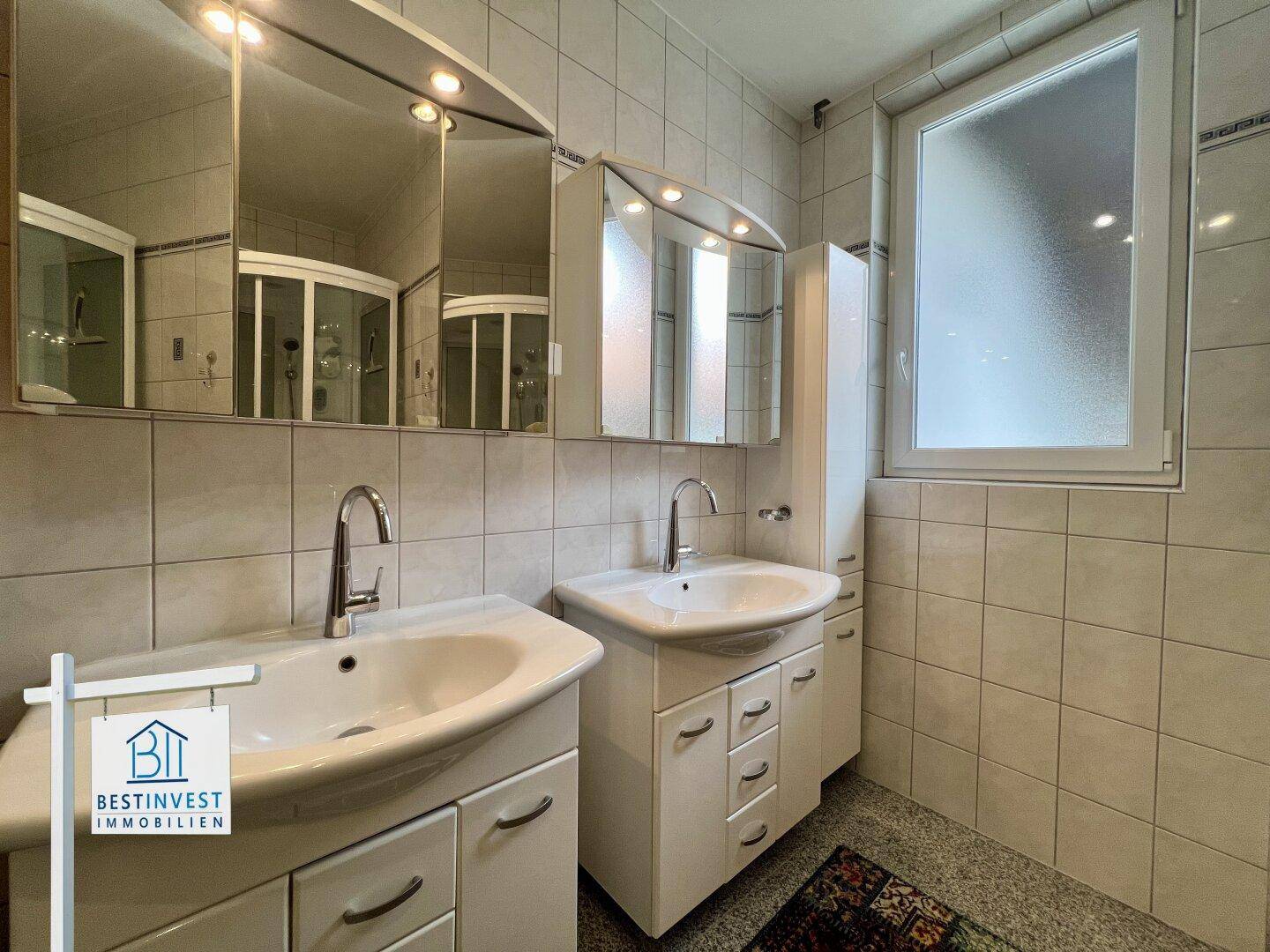Modernes Badezimmer mit Doppelwaschbecken, Spiegelschrank und Fenster.