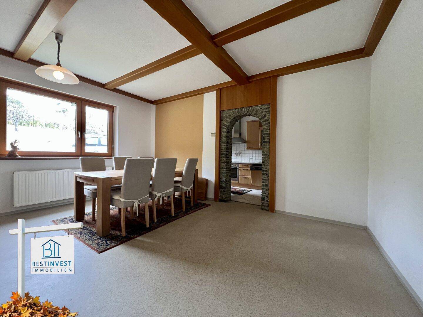 Geräumiges Esszimmer mit Holztisch, Stühlen und sichtbaren Deckenbalken, angrenzend an die Küche.