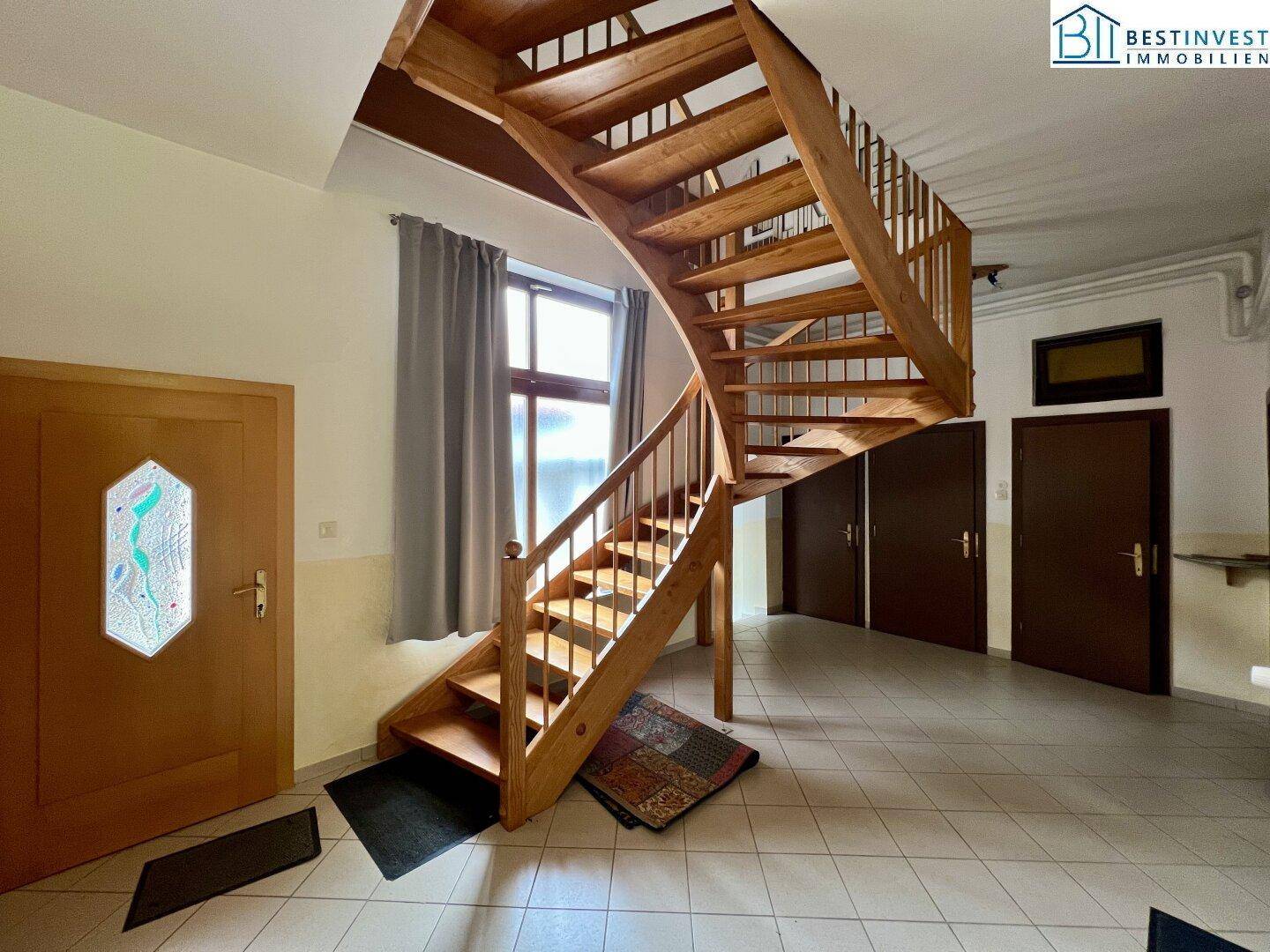 Heller Eingangsbereich mit einer eleganten Holztreppe und Fliesenboden, der zu den oberen Etagen führt.