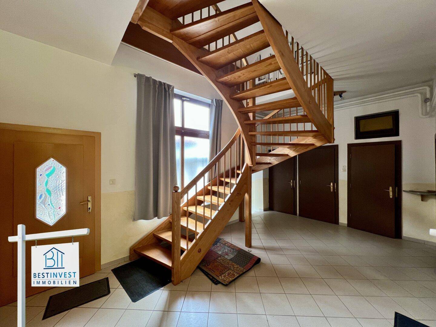 Heller Eingangsbereich mit einer eleganten Holztreppe und Fliesenboden.