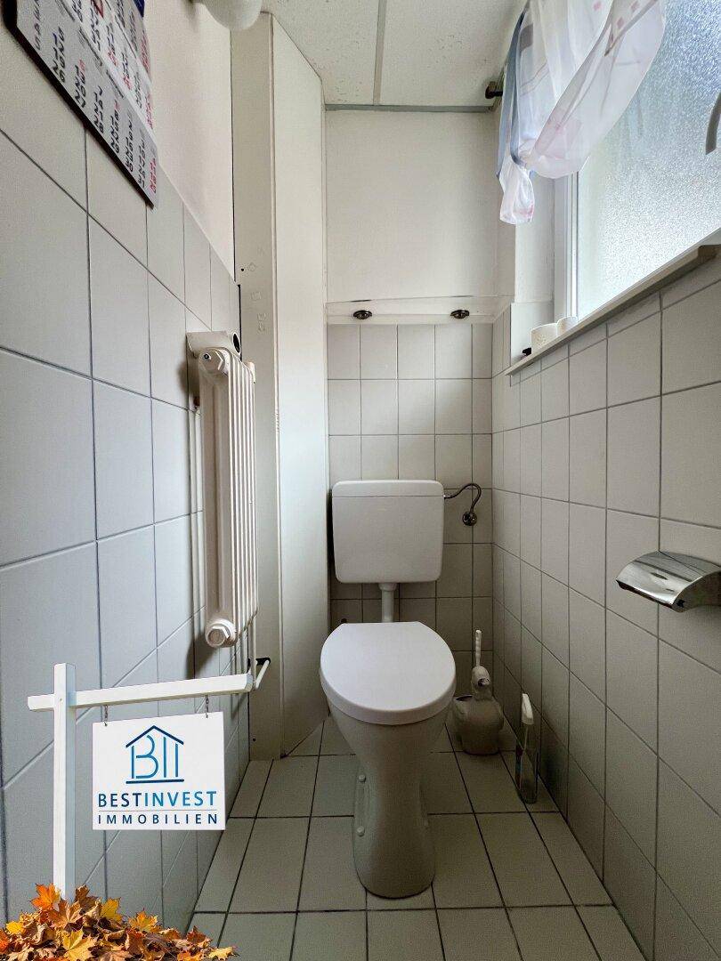 Kleines Gäste-WC mit Fliesenboden, WC, Heizkörper und einem kleinen Fenster.
