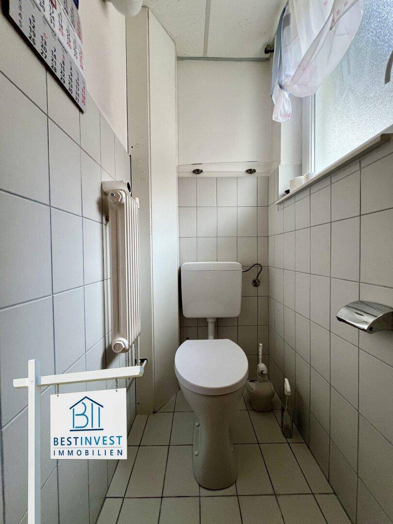 Kleines Gäste-WC mit weißen Fliesen, Fenster und Heizkörper.
