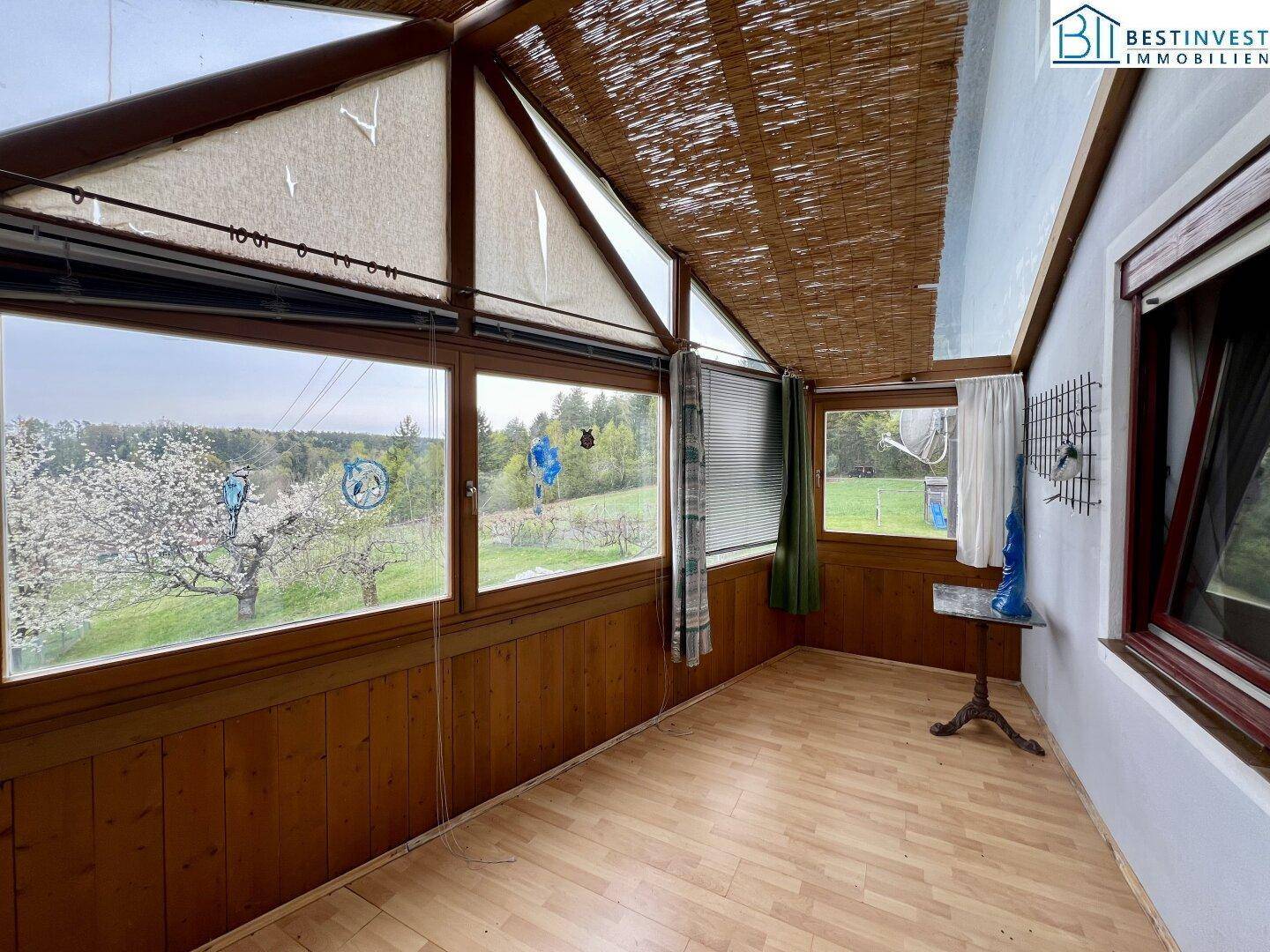 Gemütlicher Wintergarten mit Holzverkleidung und großen Fenstern, bietet einen schönen Ausblick ins Grüne.