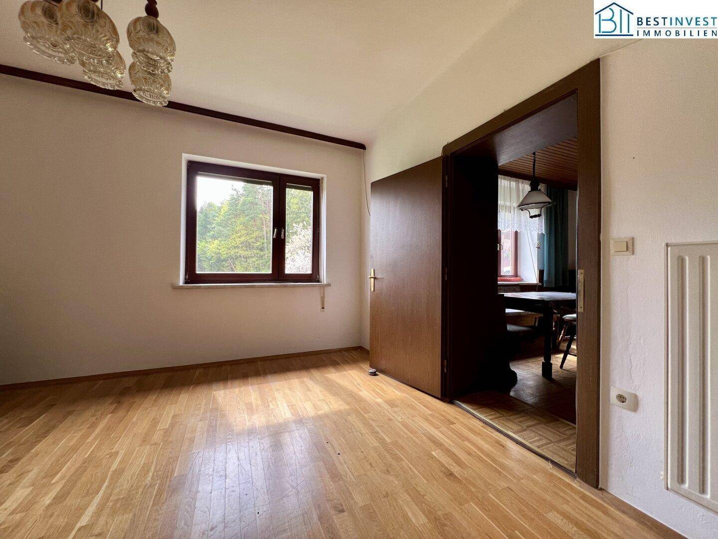 Helles Zimmer mit Holzboden und einer Tür, die zu einem weiteren Raum führt, ideal als Schlafzimmer.