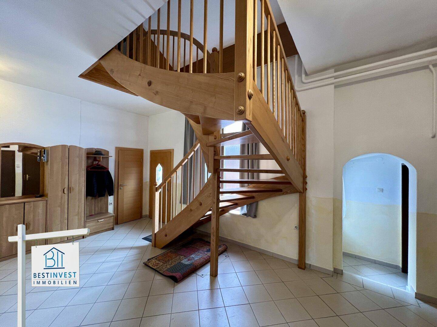 Geräumiger Eingangsbereich mit einer markanten Holzwendeltreppe und Fliesenboden.