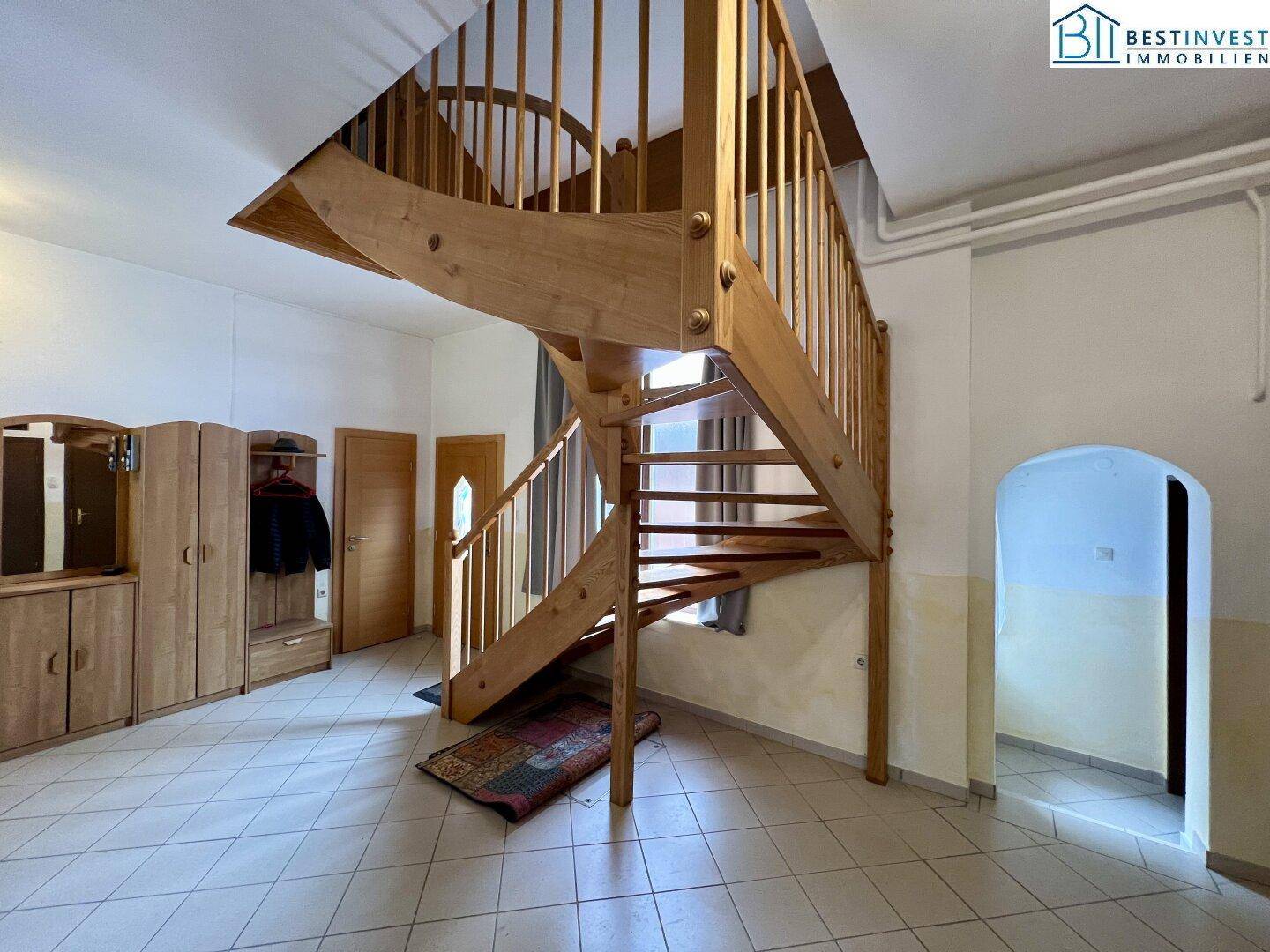 Heller Eingangsbereich mit einer eleganten Holztreppe und Fliesenboden, die das Obergeschoss erschließt.