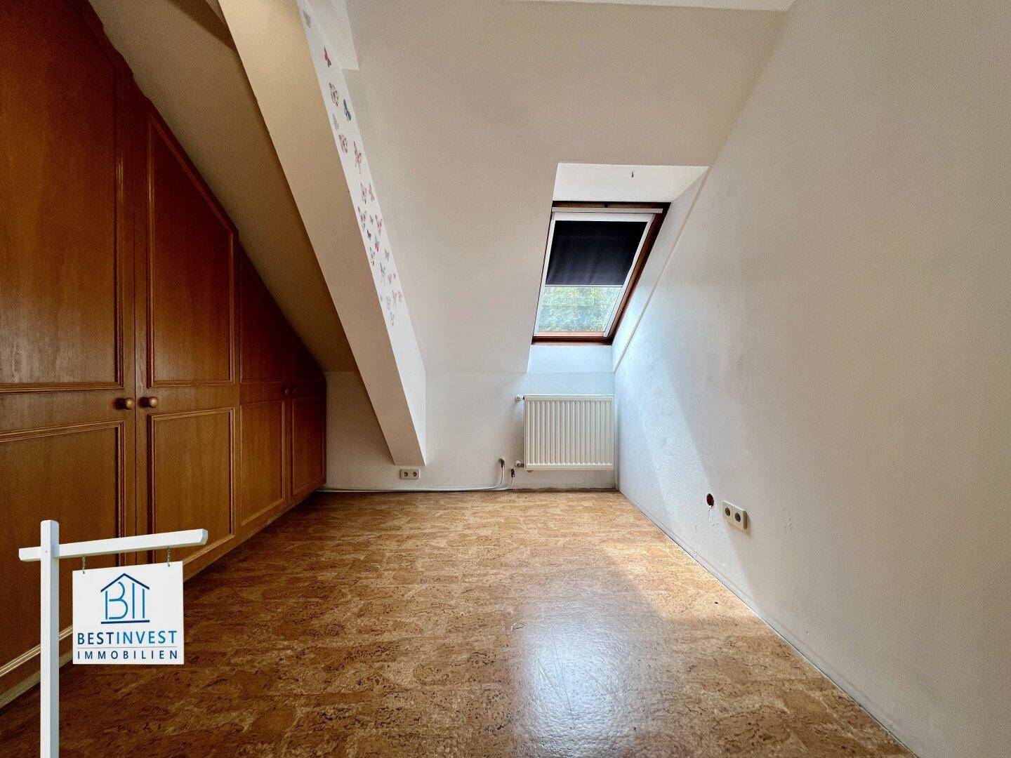 Schlafzimmer mit Dachschrägen, Einbauschränken aus Holz und einem Dachfenster für Tageslicht.