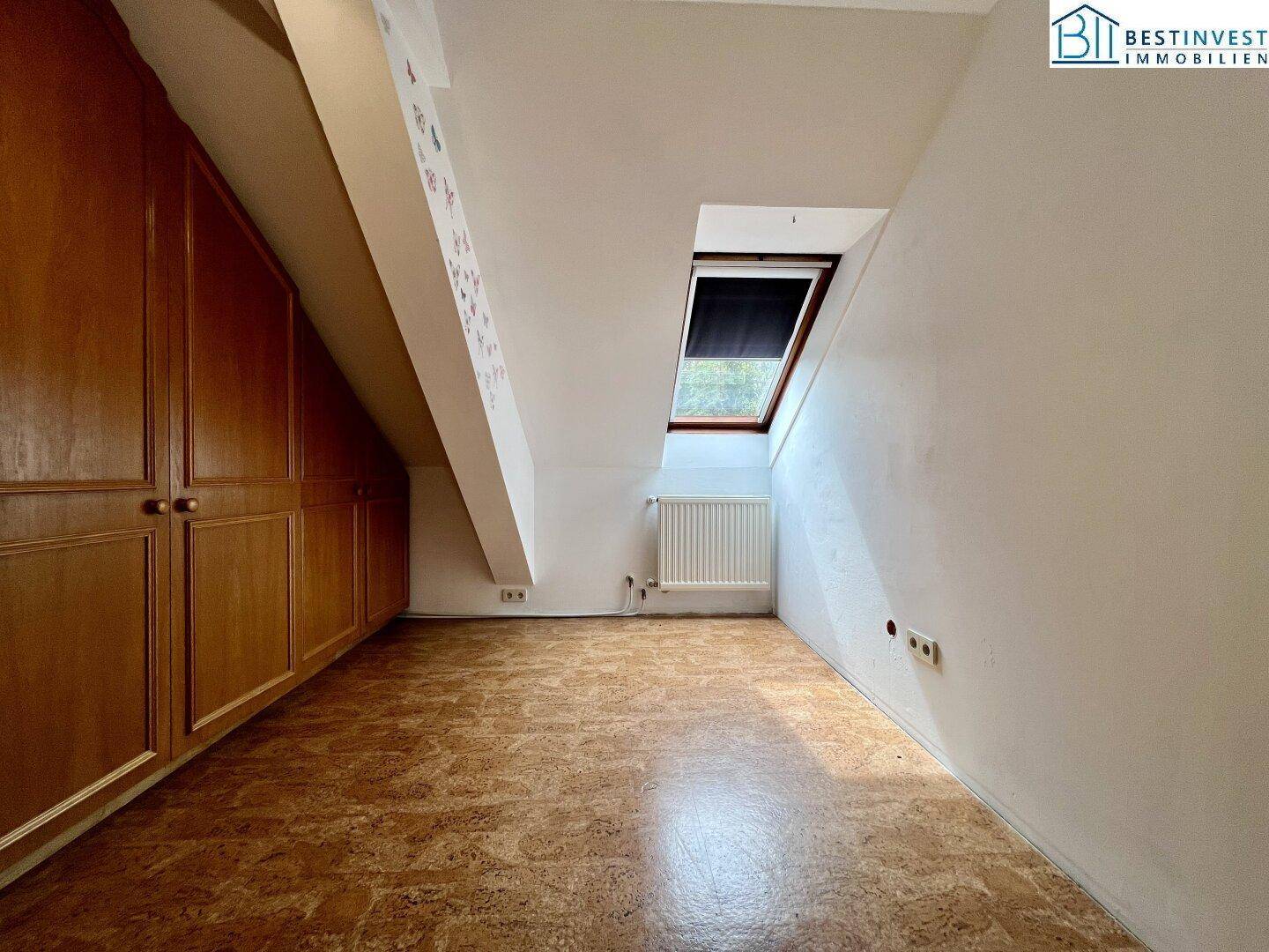 Geräumiges Zimmer im Dachgeschoss mit Einbauschränken und Dachfenster, ideal als Schlaf- oder Arbeitszimmer.