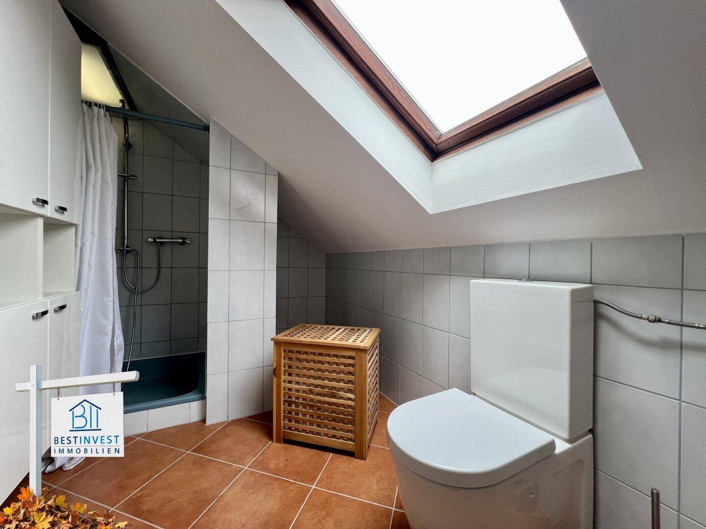 Badezimmer im Dachgeschoss mit Dusche, WC und einem Dachfenster für natürliches Licht.