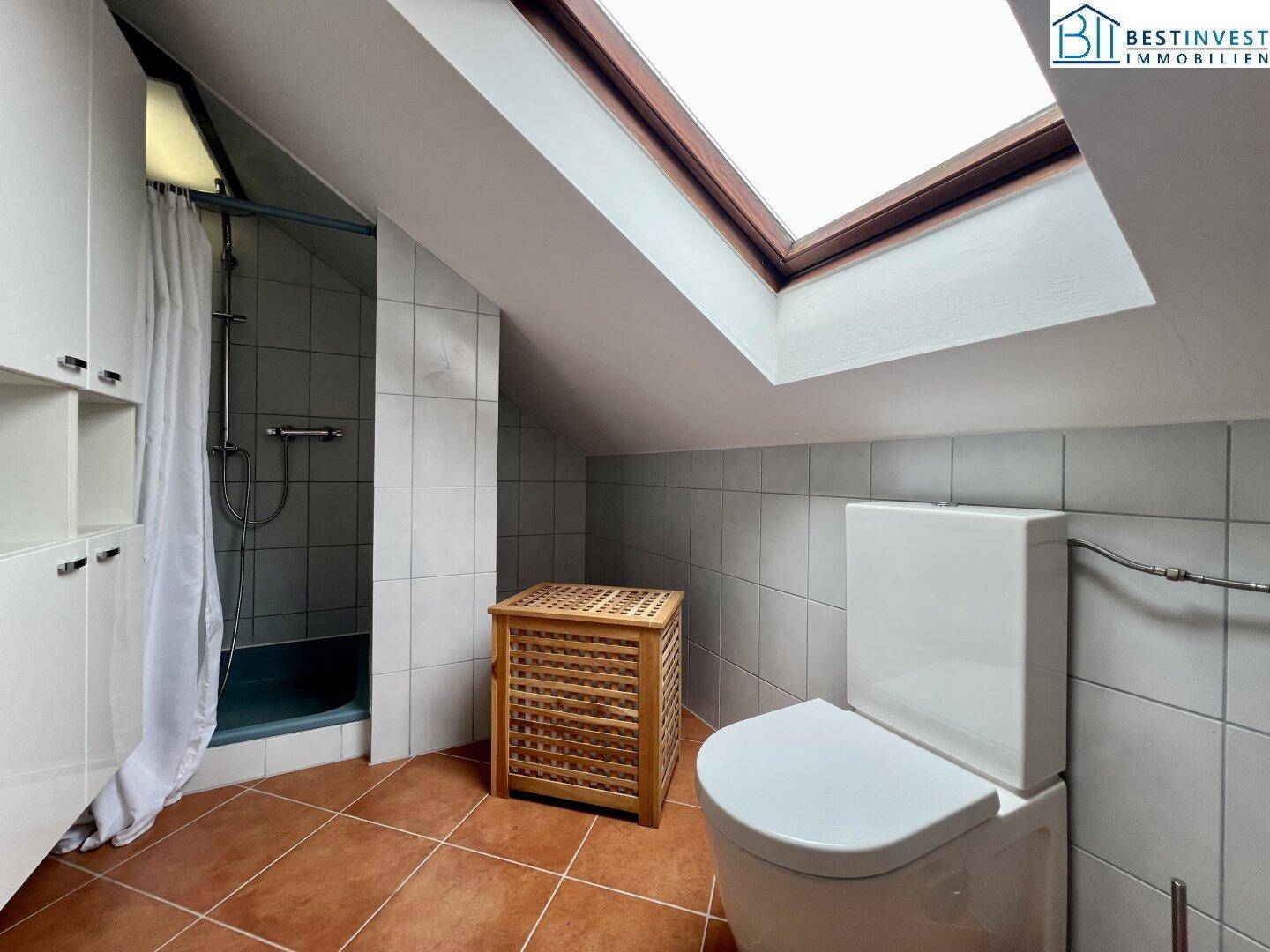 Badezimmer im Dachgeschoss mit Dusche, WC und Dachfenster, bietet ausreichend Tageslicht.