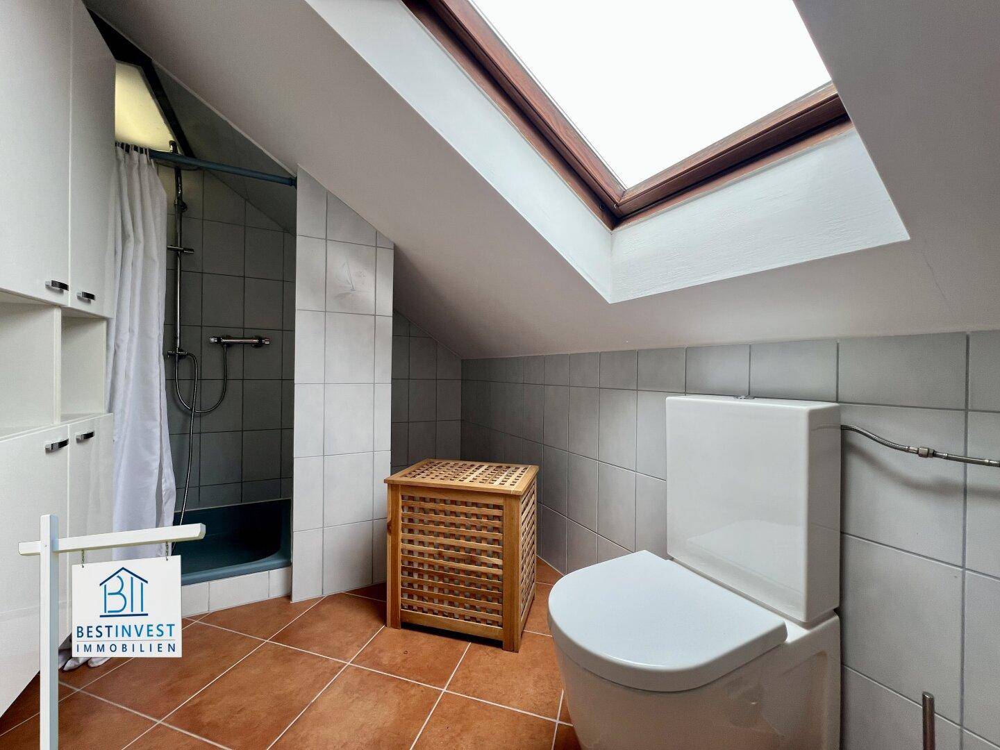 Badezimmer im Dachgeschoss mit Dusche, WC, Fliesenboden und einem großen Dachfenster für natürliches Licht.